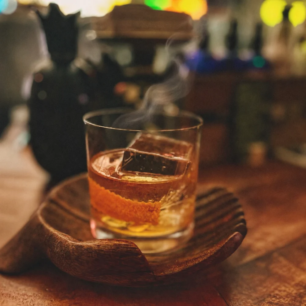 Cóctel Old Fashioned de McCoy con humo sutil, servido en vaso bajo